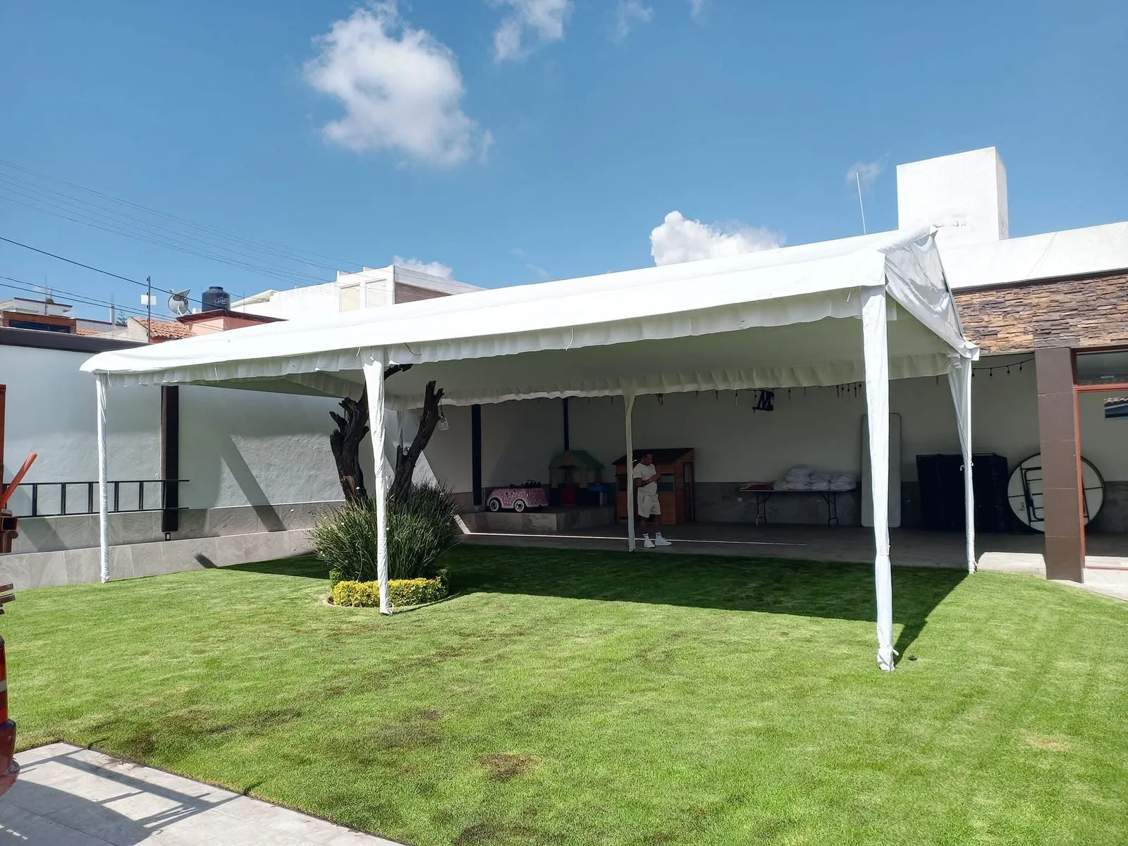 Carpa blanca unida a la construcción de una casa, cubriendo jardín y porche